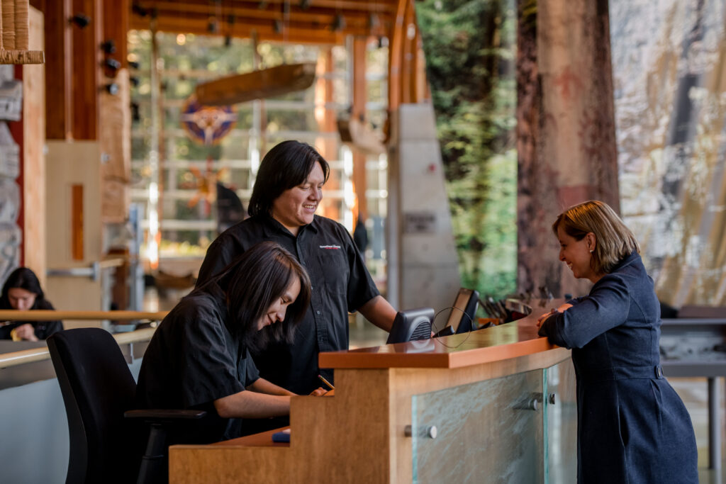 Two workers at an Indigenous information centre helping a guest standing on the opposite side of the desk.