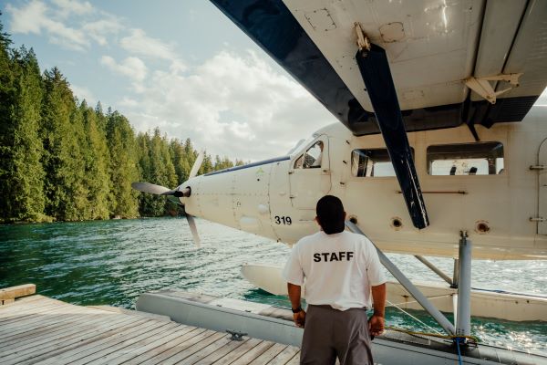 Male looking at a sea plane wearing a shirt that has the word "Staff" on the back in block letters.