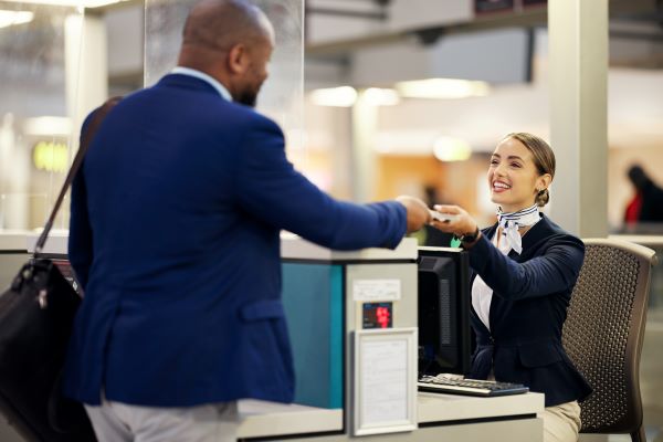 An airline ticket agent seated at the checkin counter hands a passport back to a traveller.