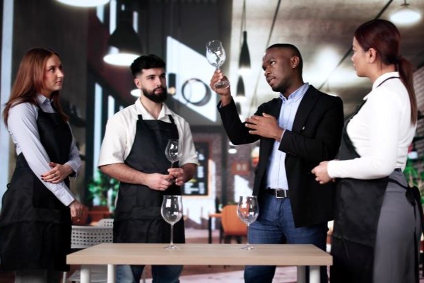 A restaurant manager teaches three staff members how to inspect glassware.