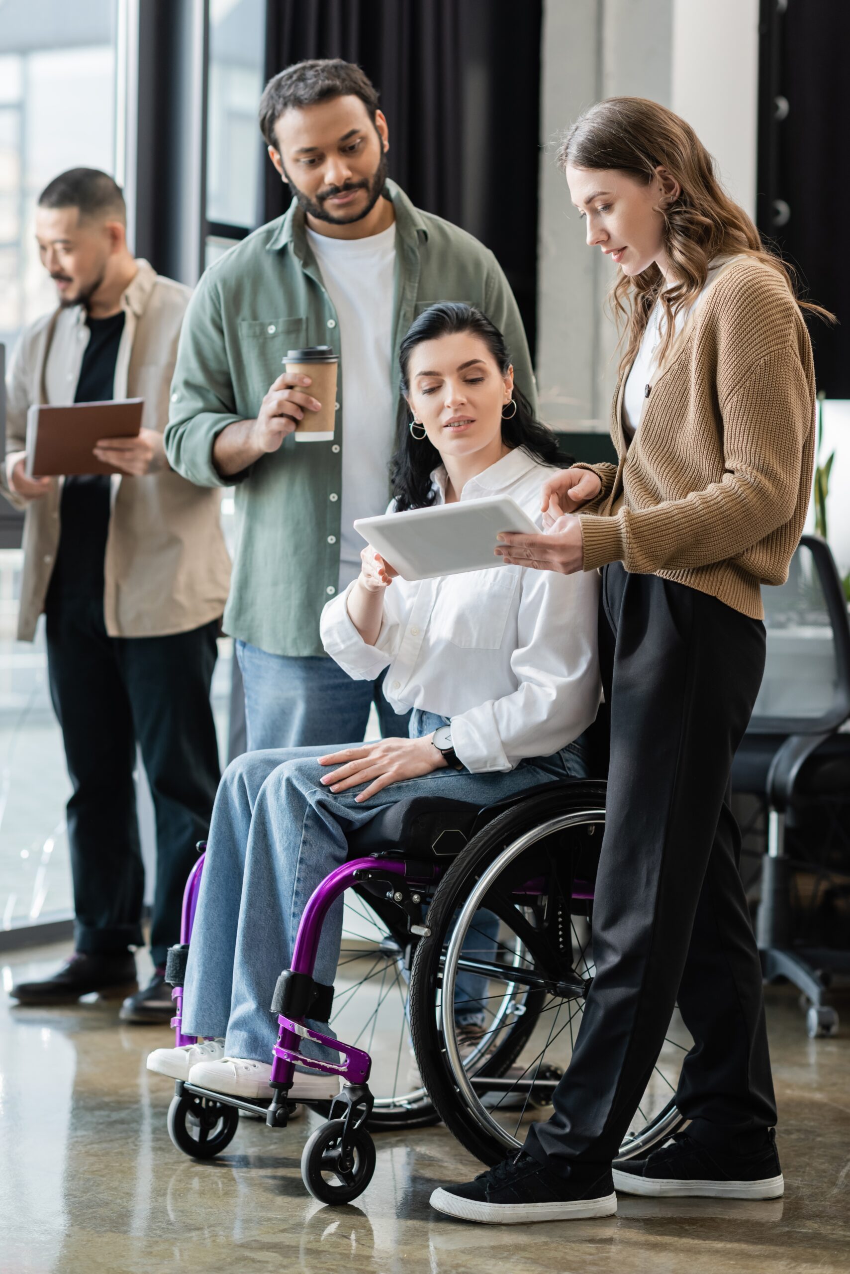 Group of professionals looking a tablet. One female is using a wheelchair.