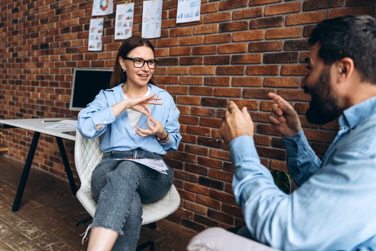A man and woman are seated in an office, having a conversation using sign language.