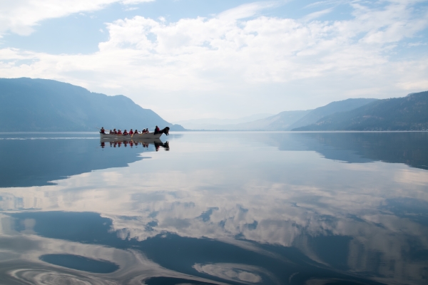 Scenic landscape on water with mountains in the horizon with a blue sky. There is a canoe floating across the water with people in it.