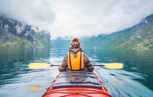 Girl in a canoe wearing a life jacket. She is facing the mountains and open water.