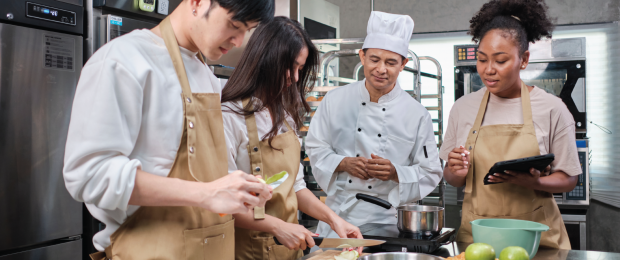 Group of young chefs working with an overseeing chef beside them
