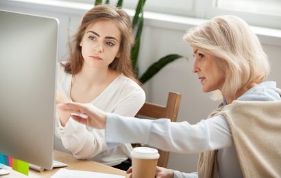 Two females sat around a computer screen. The older of the females is pointing to the computer screen.