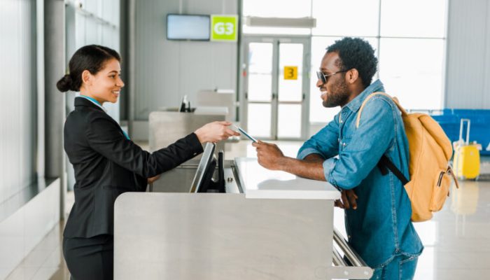 Female airline front desk attendant handing a boarding pass to a male guest. They are both smiling.