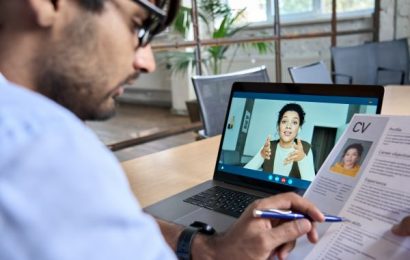 Male recruitor on a video call with a prospect who is on the laptop screen. He is holding a Resume of the prospect.