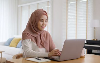 Female wearing a hijab sitting at home, working on her laptop.