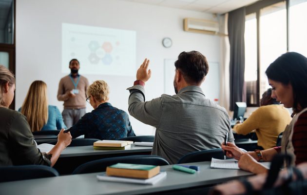 Rear View Of Man Raising Arm To Ask A Question