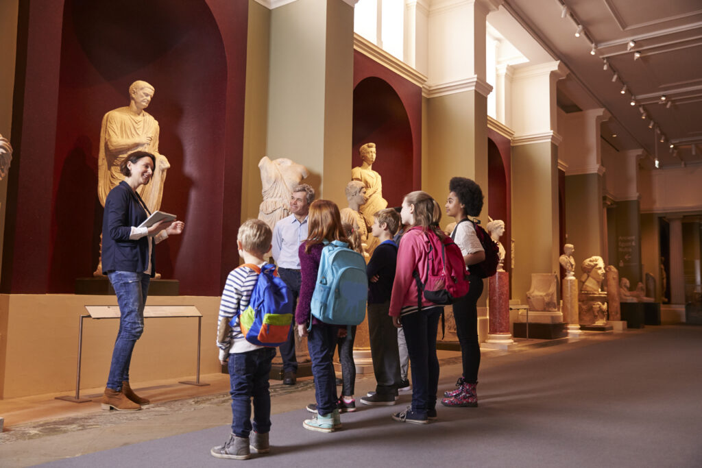 Female museum tour guide showing a group of young students around the museum exhibit