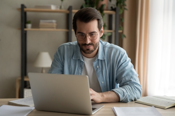 A man sits at a desk at home, using a laptop.