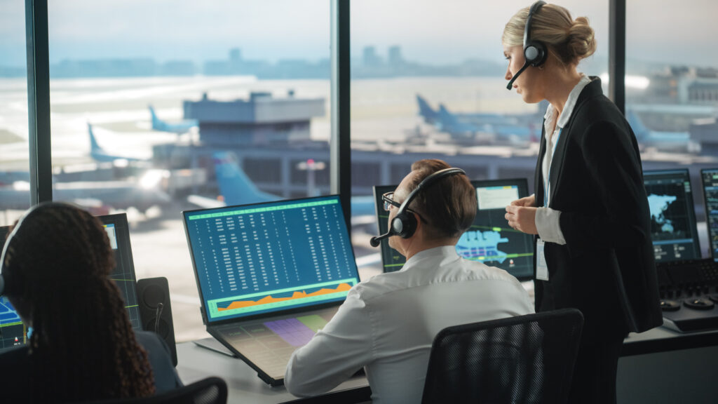 Two Air Traffic Controller workers looking at a computer screen. They are both wearing headsets.