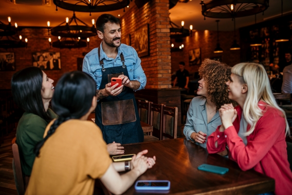 A server at a restaurant smiles and interacts with a table of four people.