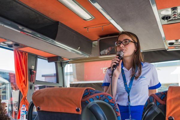 Tour guide on a bus speaks into a handheld microphone.